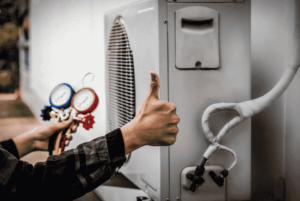 Technician giving a thumbs-up while servicing an outdoor HVAC unit, checking pressure gauges for HVAC refrigerants to ensure optimal performance and system efficiency.