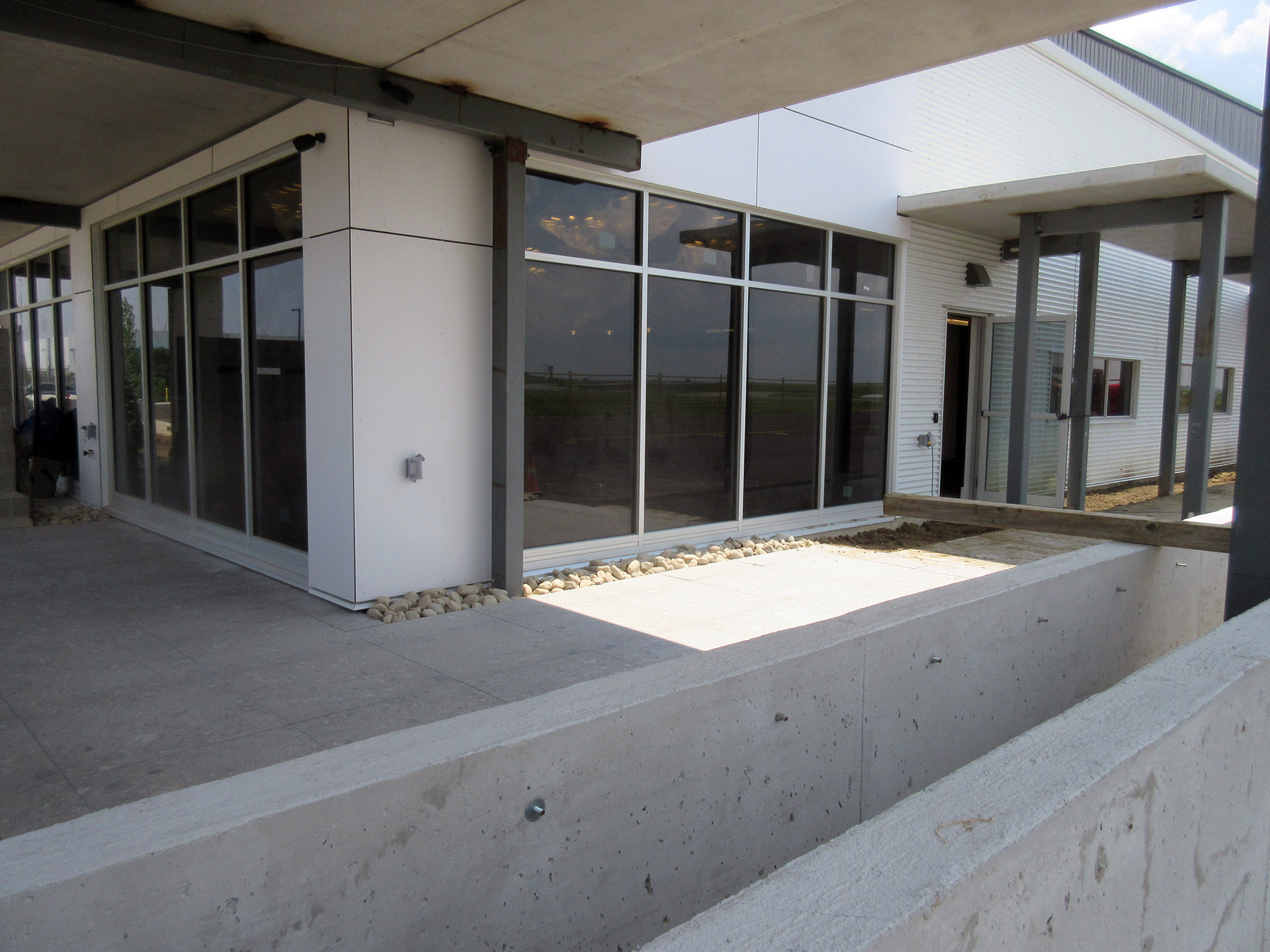 Latitude Air Ambulance 10 Exterior corner of the Latitude Air Ambulance facility with white cladding, floor‑to‑ceiling windows, and a concrete walkway beneath a canopy.