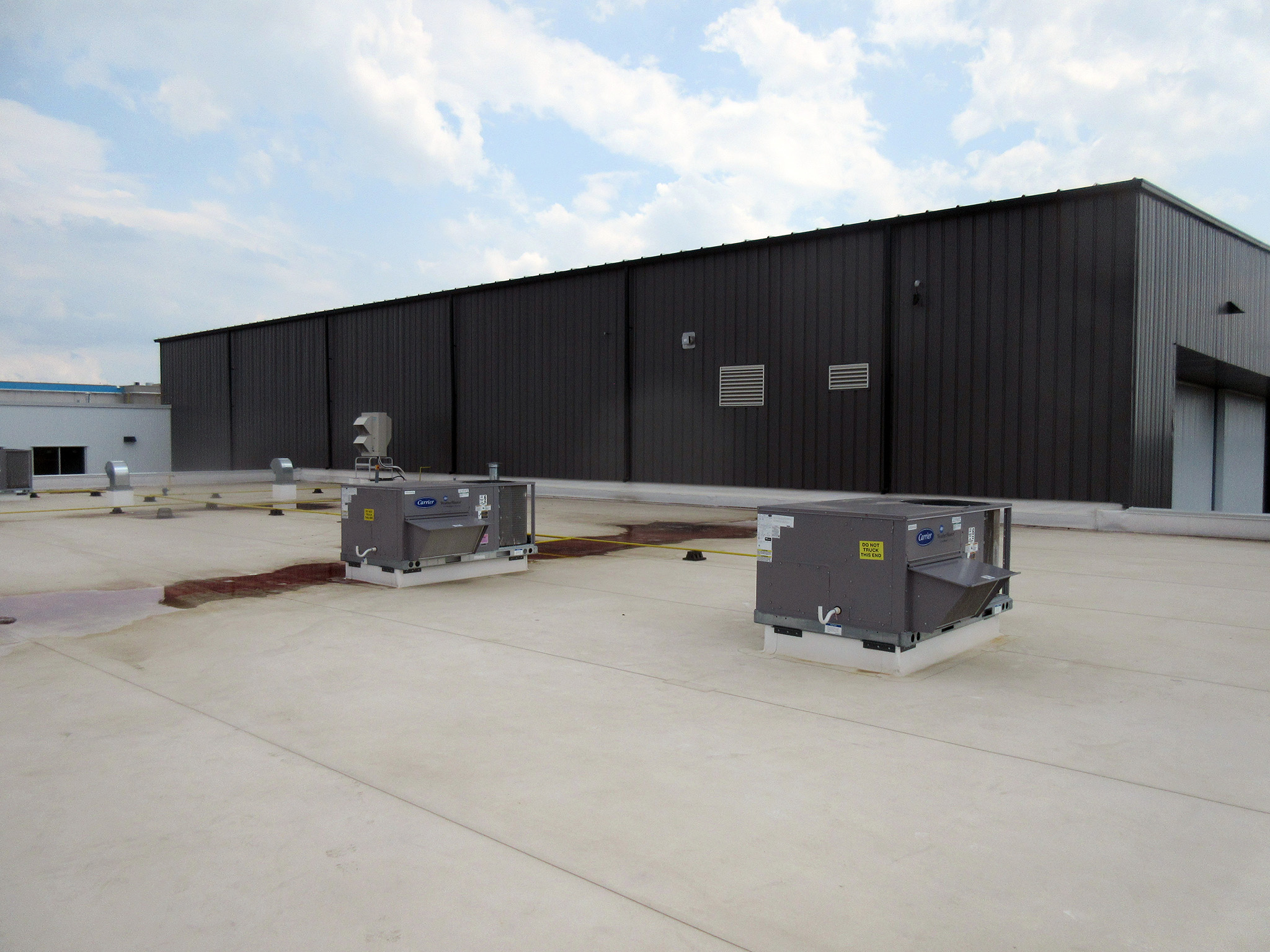 Latitude Air Ambulance 18 Flat roof of the Latitude Air Ambulance hangar with two grey Carrier rooftop HVAC units and ventilation ducts beside a dark metal wall.