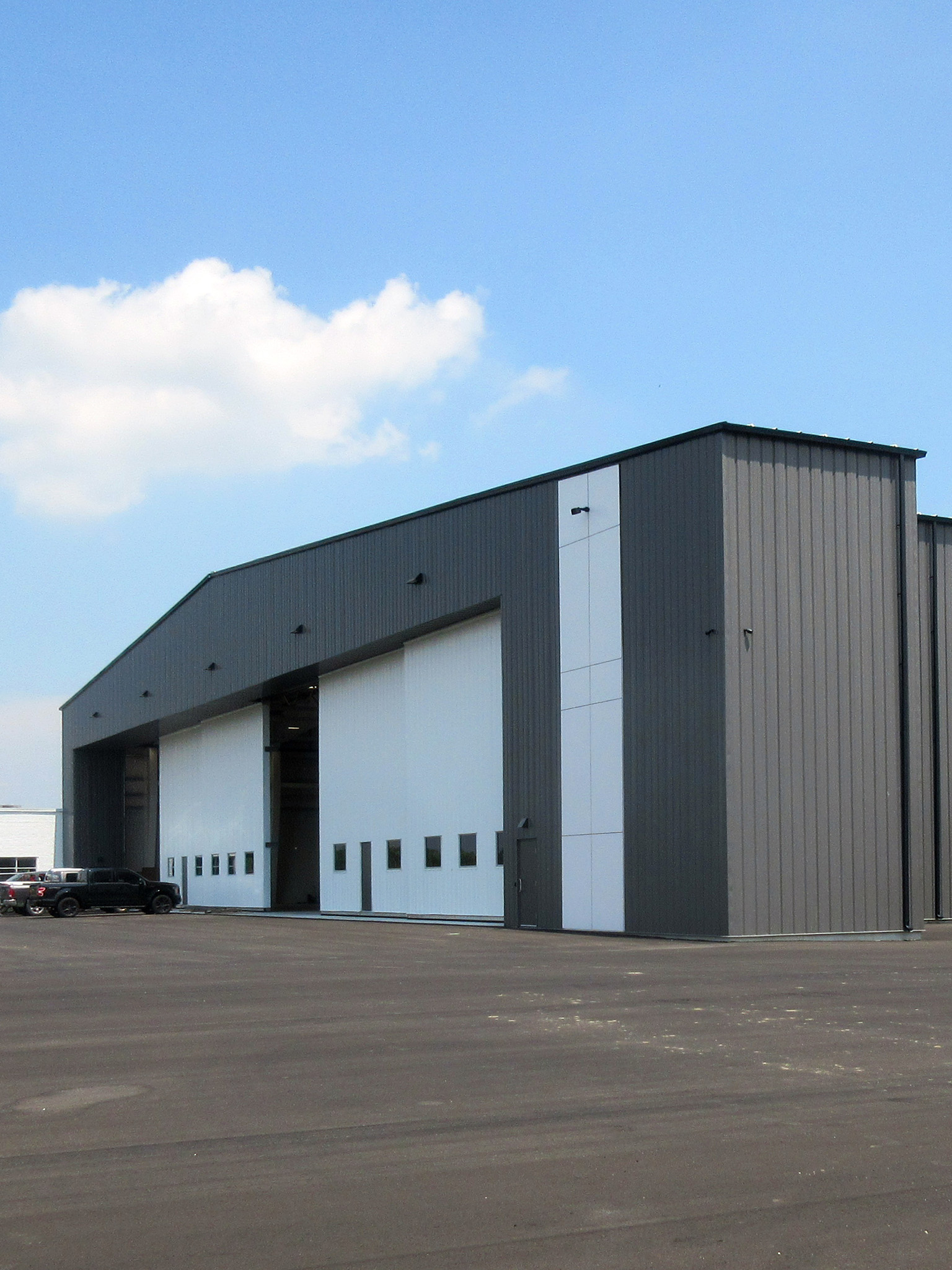 Latitude Air Ambulance 2 Latitude Air Ambulance’s grey steel aircraft hangar at Hamilton International Airport, featuring large white sliding doors that open onto the tarmac.