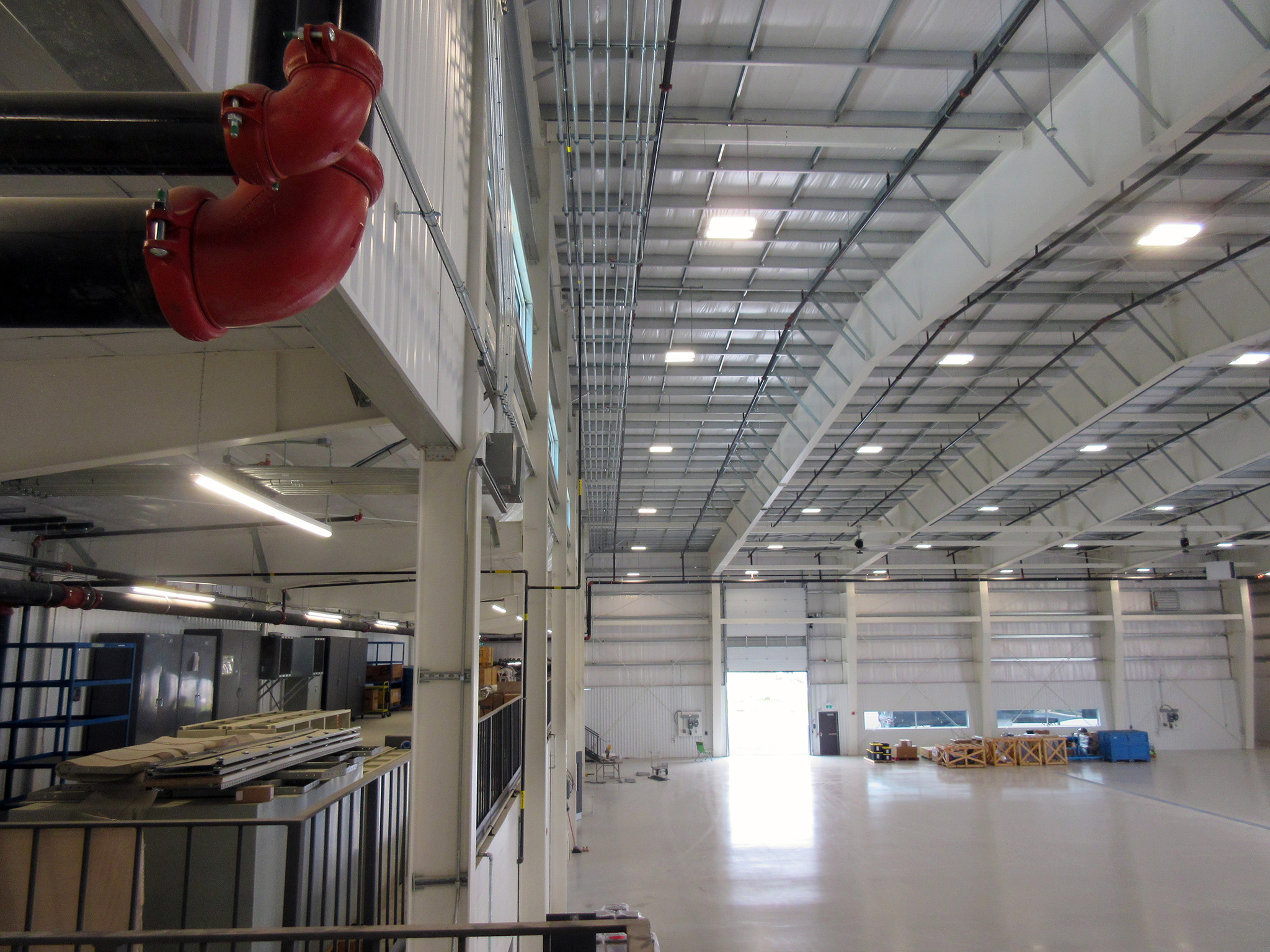 Latitude Air Ambulance 3 Interior of Latitude Air Ambulance hangar, showing high white steel trusses with bright LED lighting, red fire‑suppression piping, and an open concrete floor ready for aircraft maintenance.