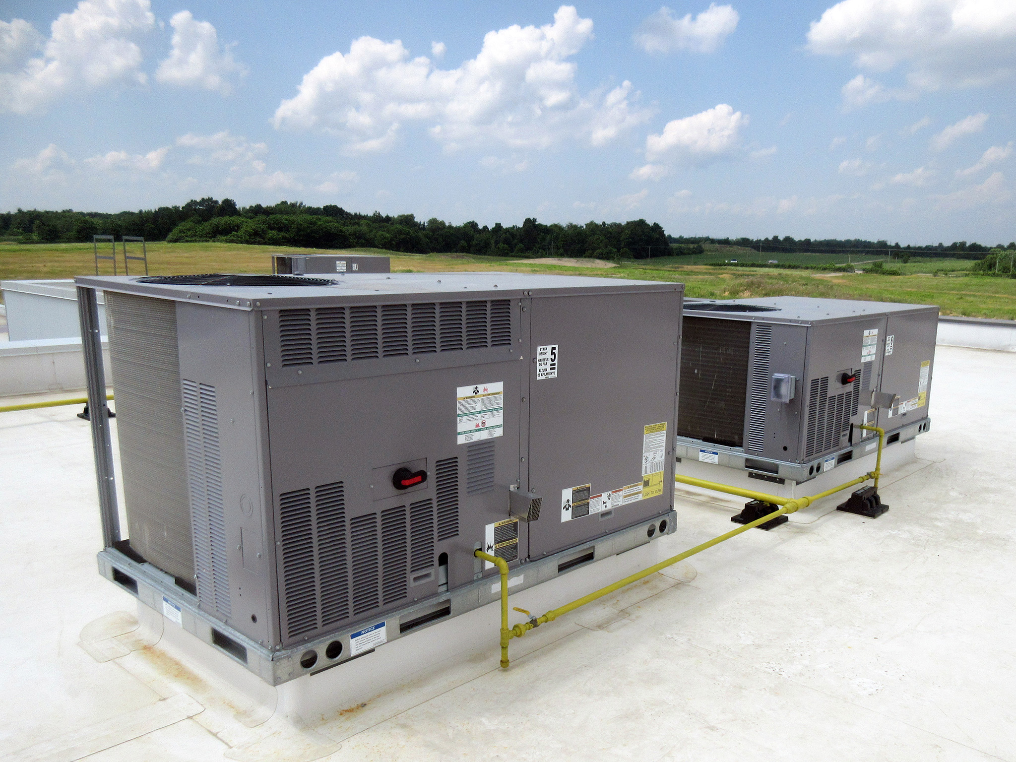 Latitude Air Ambulance 4 Two grey rooftop HVAC units on the Latitude Air Ambulance hangar, linked by yellow gas lines, with grassy airfield visible beyond.