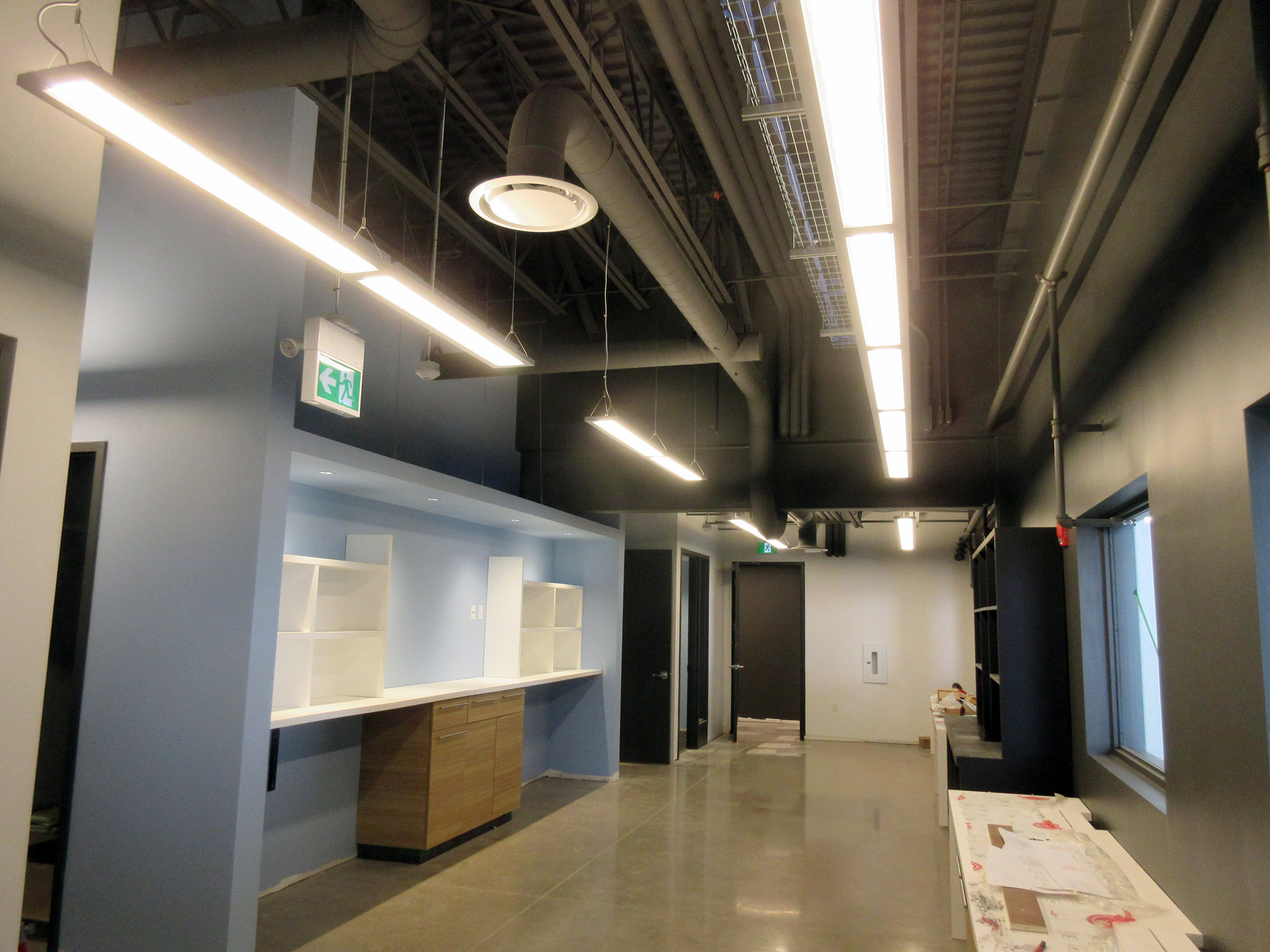 Latitude Air Ambulance 5 Interior corridor of the Latitude Air Ambulance facility, featuring exposed ductwork and suspended LED strip lights above built‑in cabinets and shelving on a polished concrete floor.