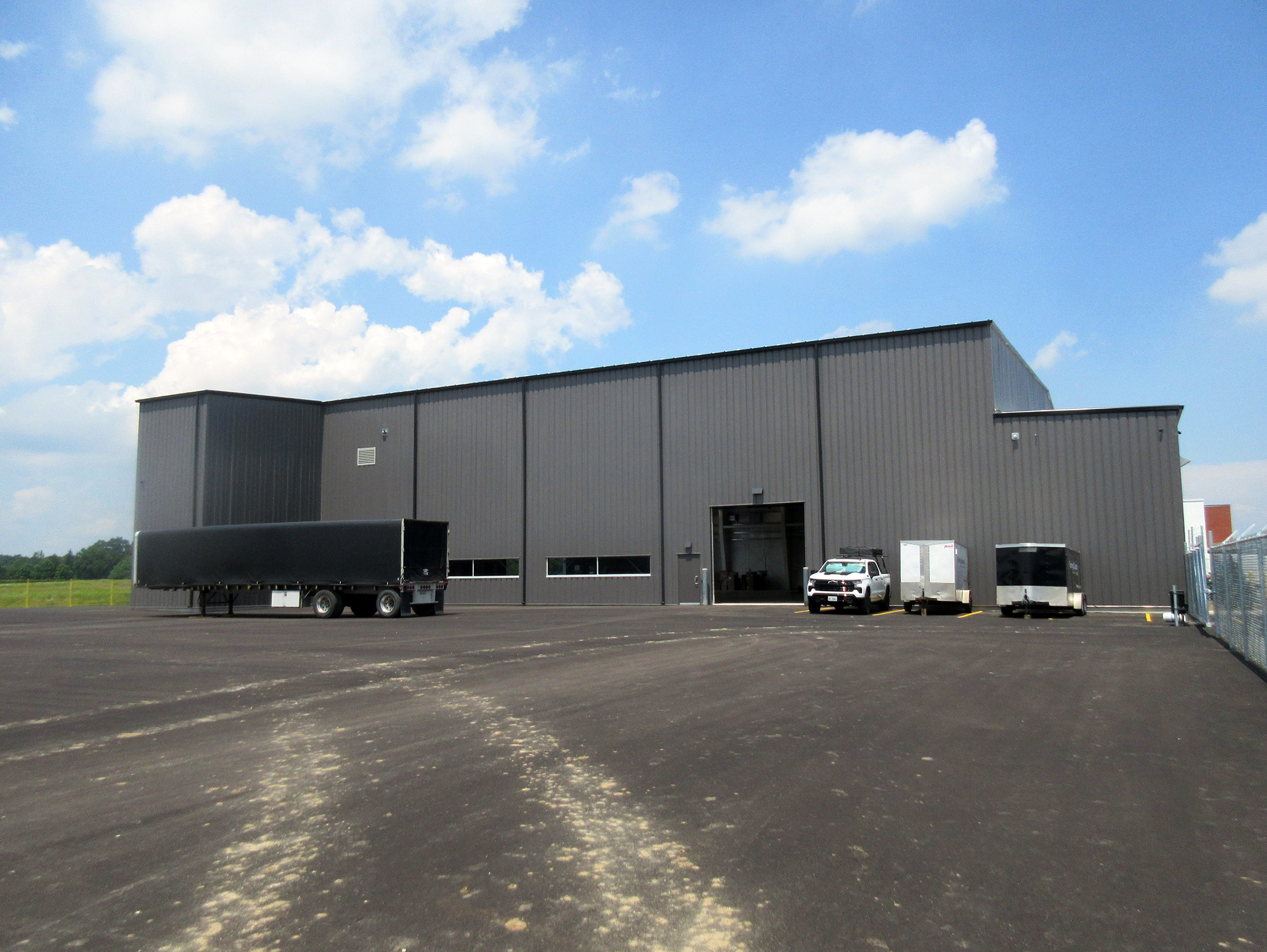 Latitude Air Ambulance 8 Rear view of the Latitude Air Ambulance hangar—a large grey steel building with a tall service door, trailers, and a pickup truck parked on the newly paved apron.