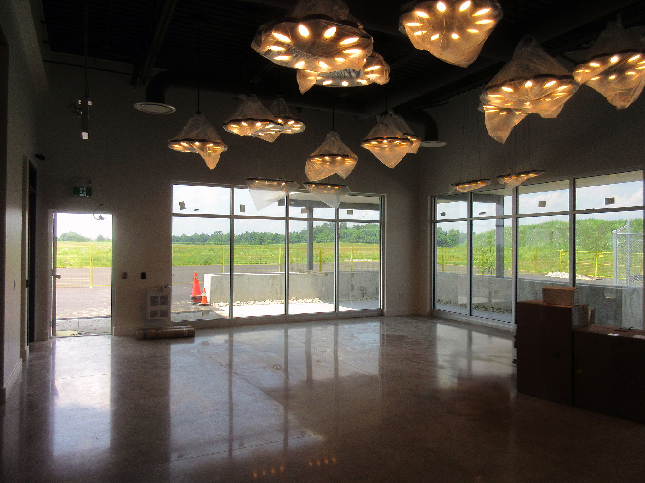 Latitude Air Ambulance 9 Lobby of the Latitude Air Ambulance facility with floor‑to‑ceiling windows, polished concrete floor, and sculptural pendant lights still wrapped in protective plastic.