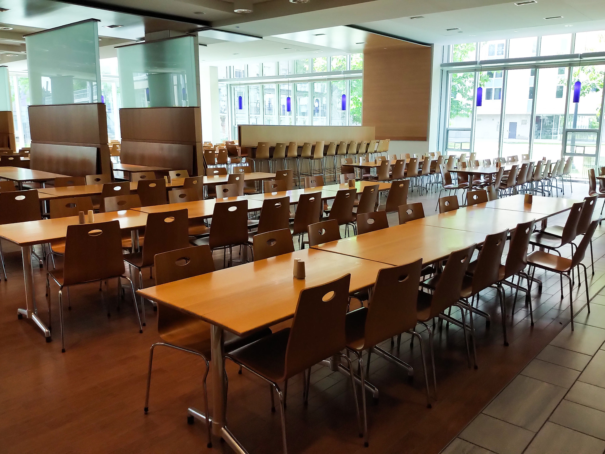 Leonard Hall 10 Interior seating area of Leonard Hall with long wooden tables and rows of brown chairs, illuminated by floor-to-ceiling windows along one wall.