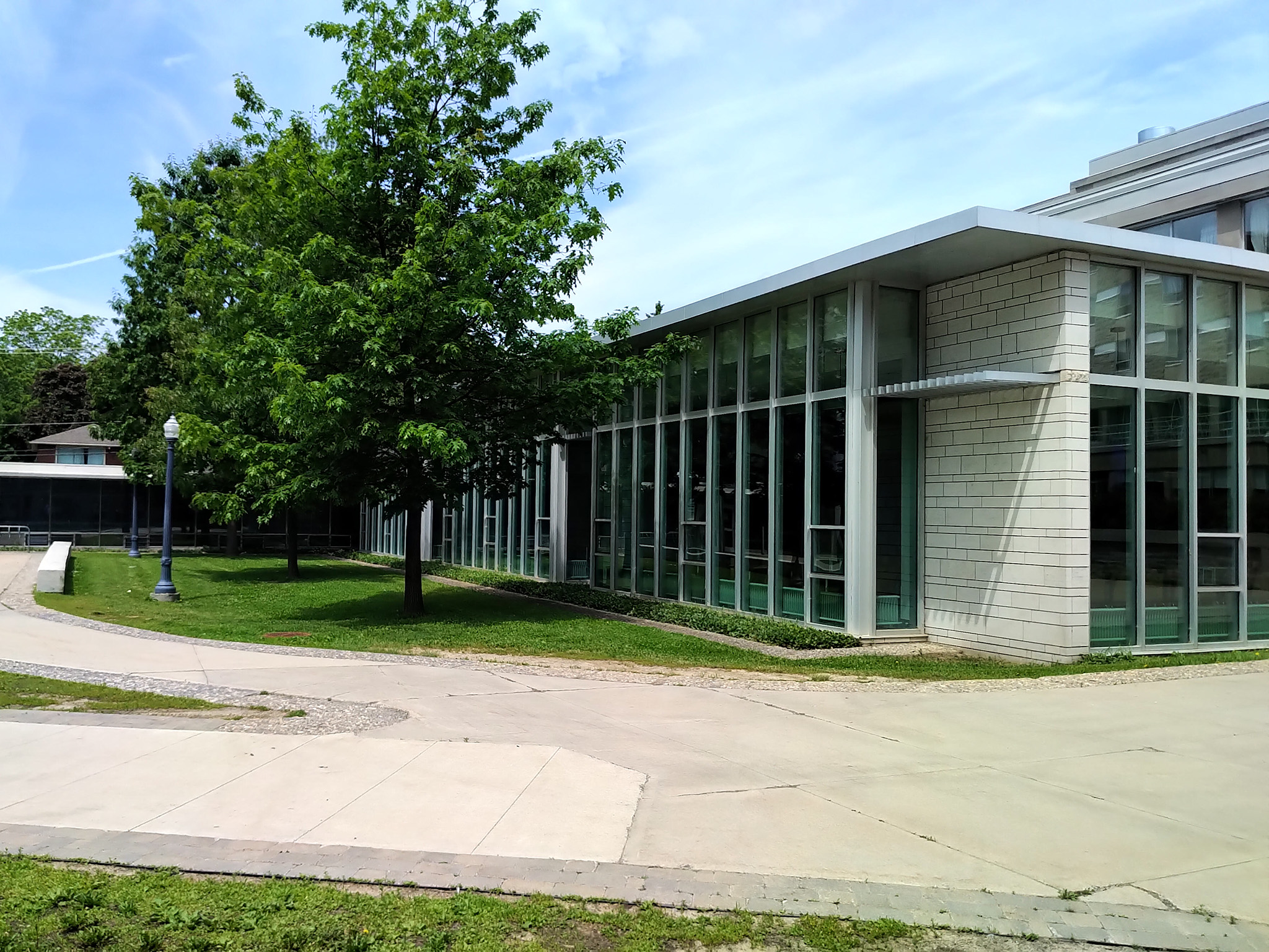 Leonard Hall 9 Exterior view of Leonard Hall’s glass-walled dining hall extension bordered by a lawn with mature trees and a curved walkway.