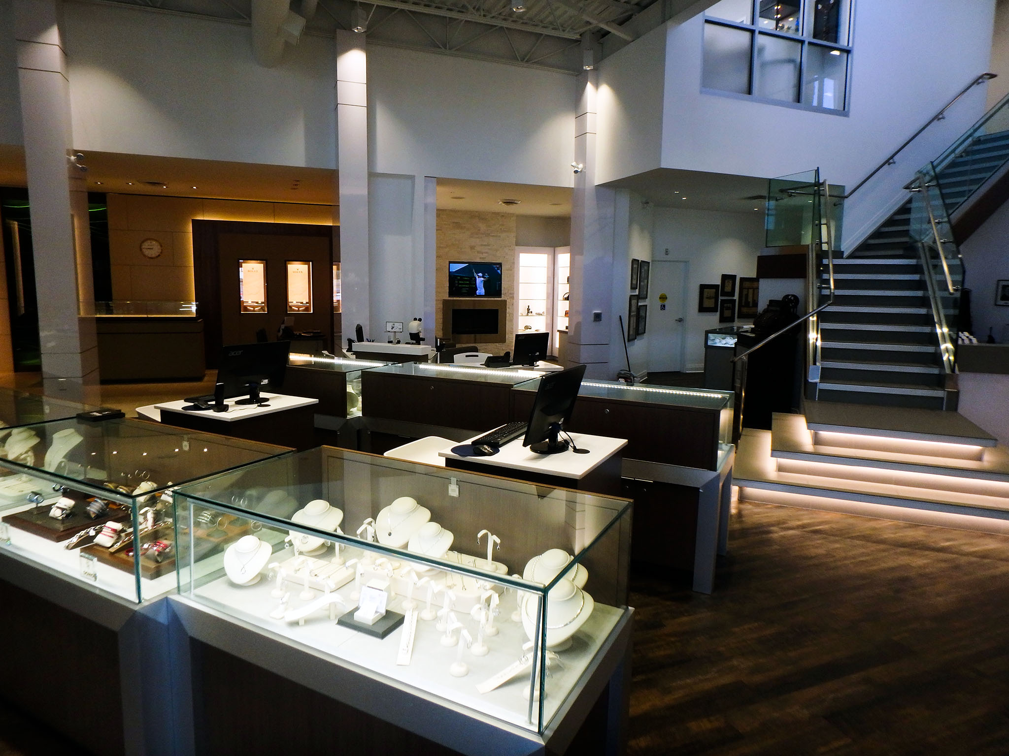 Nash Jewellers 2 Glass jewelry cases and sales desks inside Nash Jewellers showroom, with an illuminated staircase ascending to a mezzanine in the background.