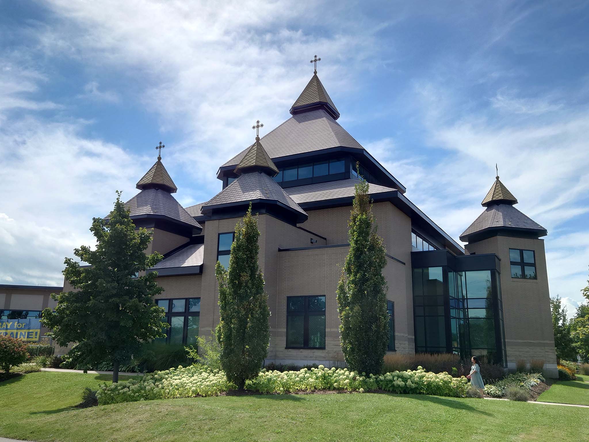 Exterior of St. Joseph’s Ukrainian Catholic Church with gold-domed towers, landscaped gardens, and a person walking along the pathway.