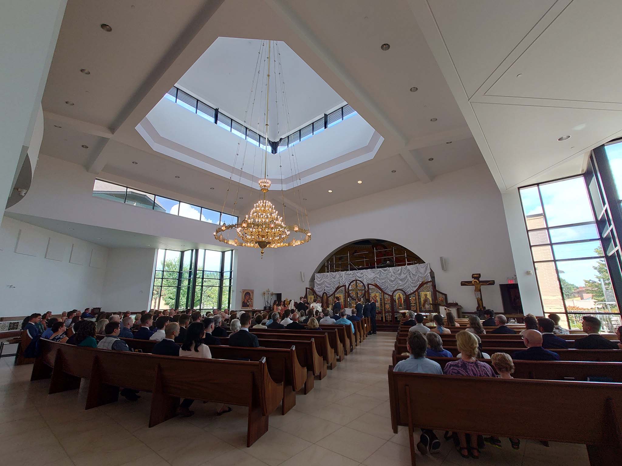Interior of St. Joseph’s Ukrainian Catholic Church during a service, showing rows of pews filled with people, a large chandelier above, and the iconostasis at the front.