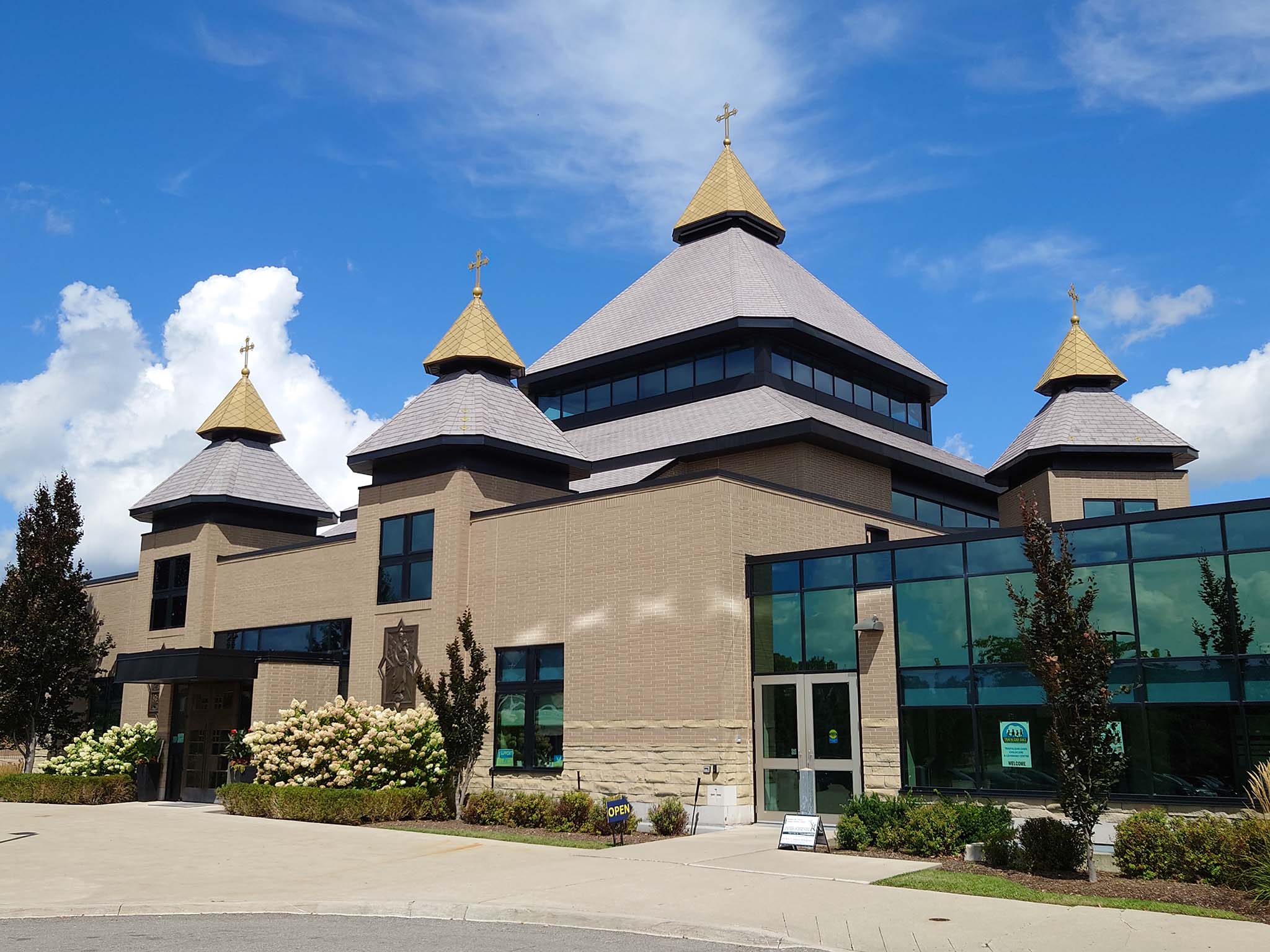Exterior view of St. Joseph’s Ukrainian Catholic Church with gold-domed towers, brick walls, and glass entrance under a bright blue sky.