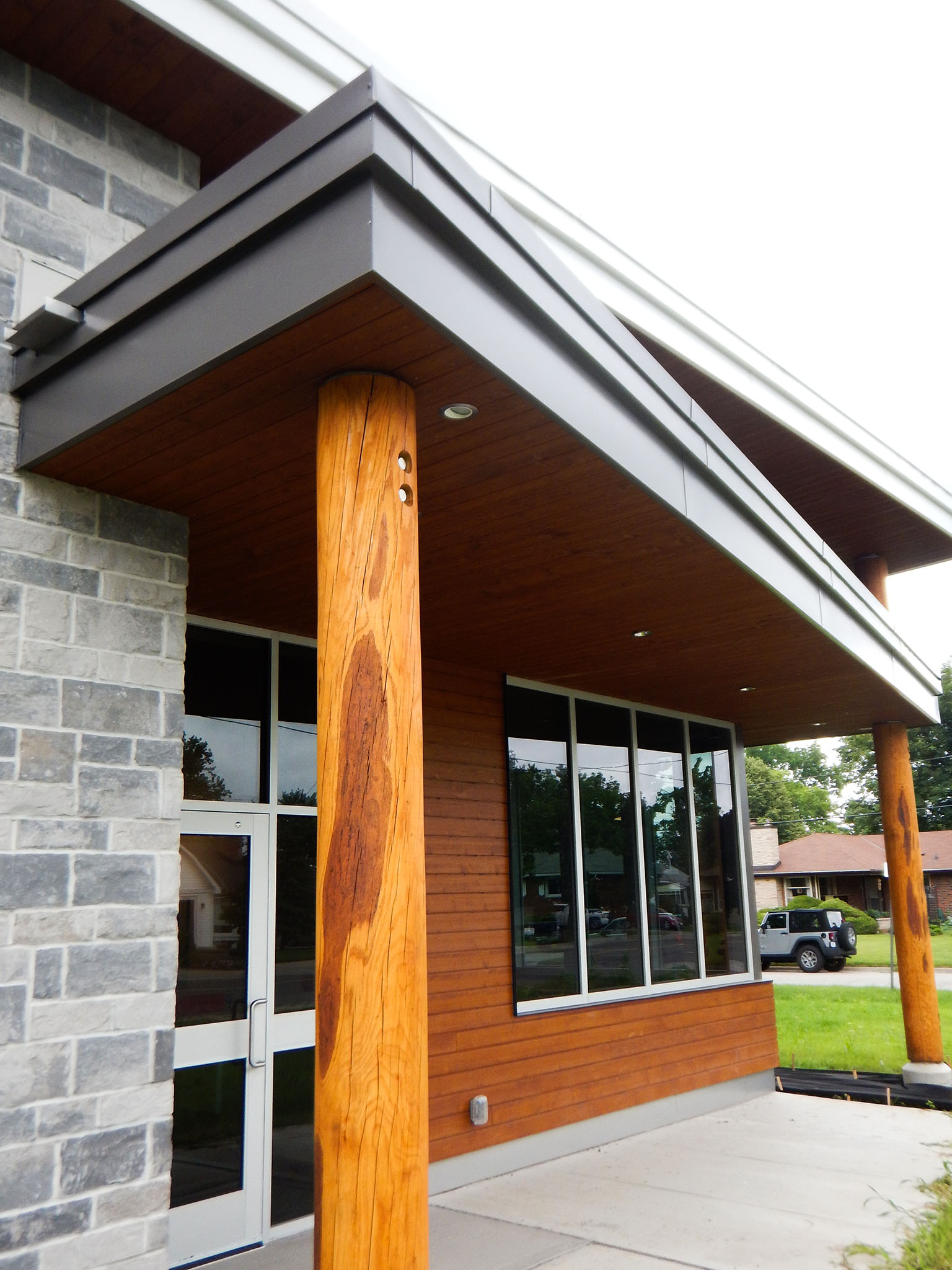 L'Arche 10 Close-up of the L’Arche Gathering Facility entrance showing wood column, stone wall, and large glass windows.