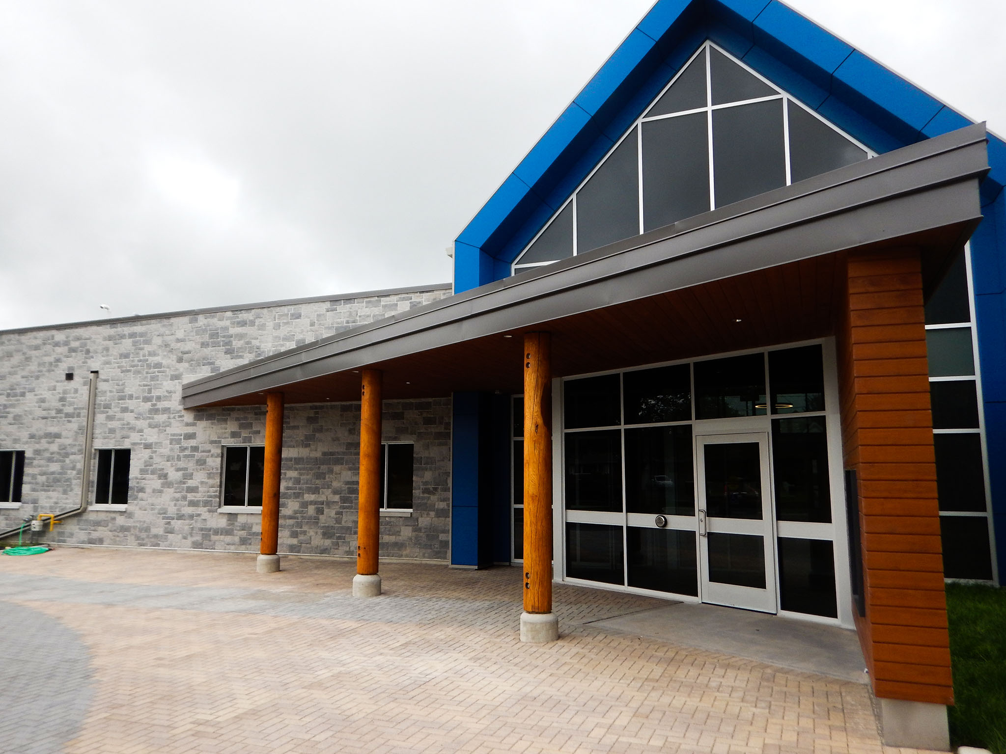 L'Arche 11 Main entrance of the L’Arche Gathering Facility with stone façade, wood columns, and tall glass gabled entry.