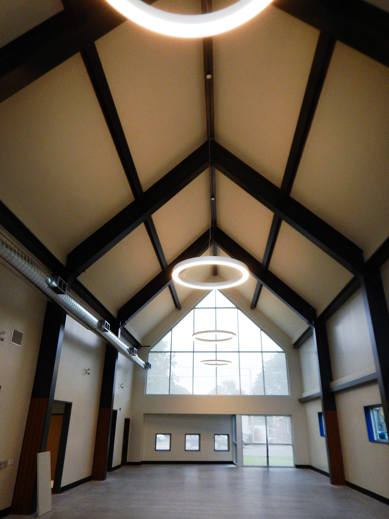 L'Arche 13 Interior of the Gathering Facility’s Great Hall with vaulted ceiling, circular LED lights, and large front windows.