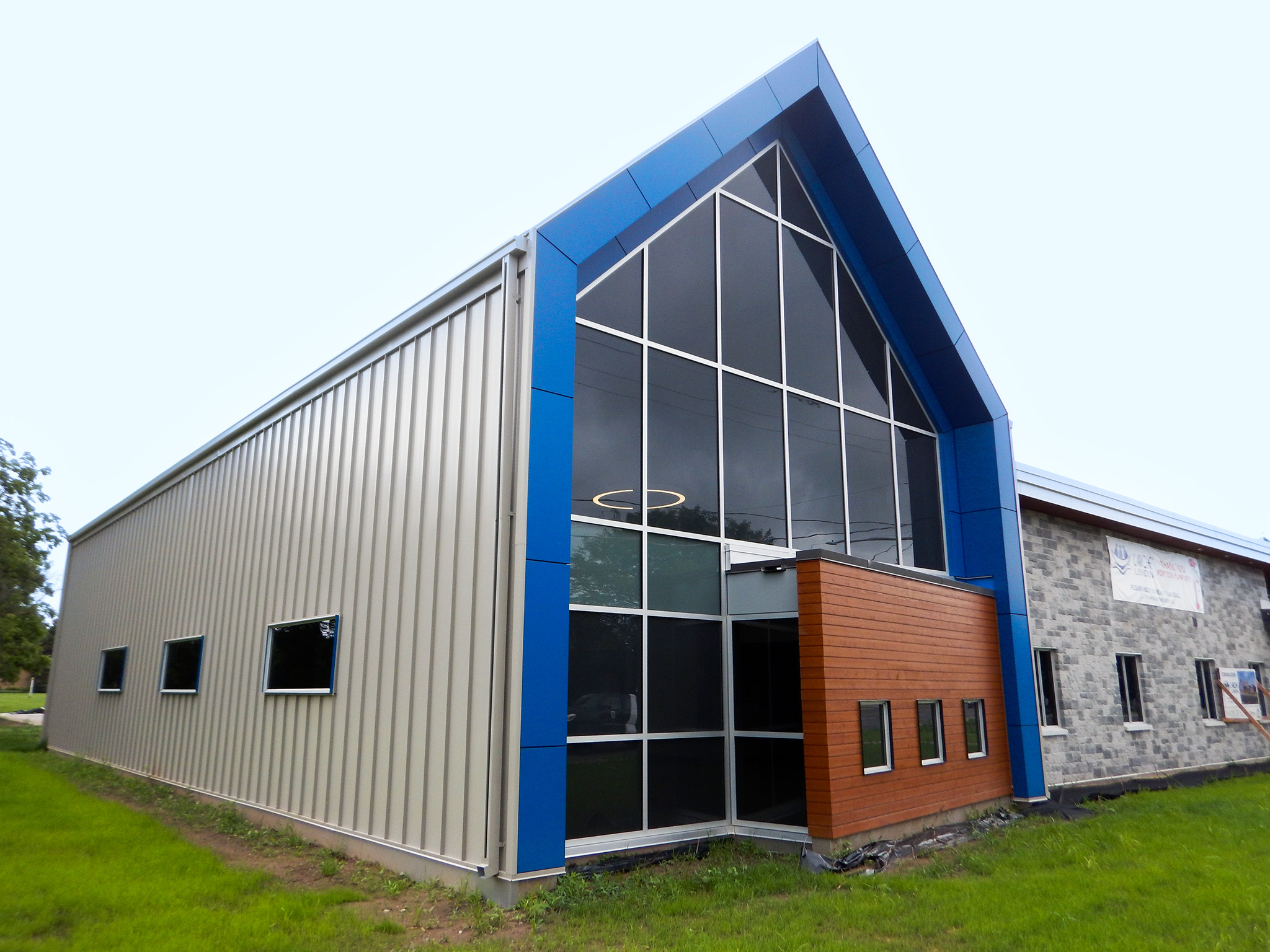 L'Arche 2 Side view of the L’Arche Community Gathering Facility with metal siding, tall glass entrance, and blue trim.