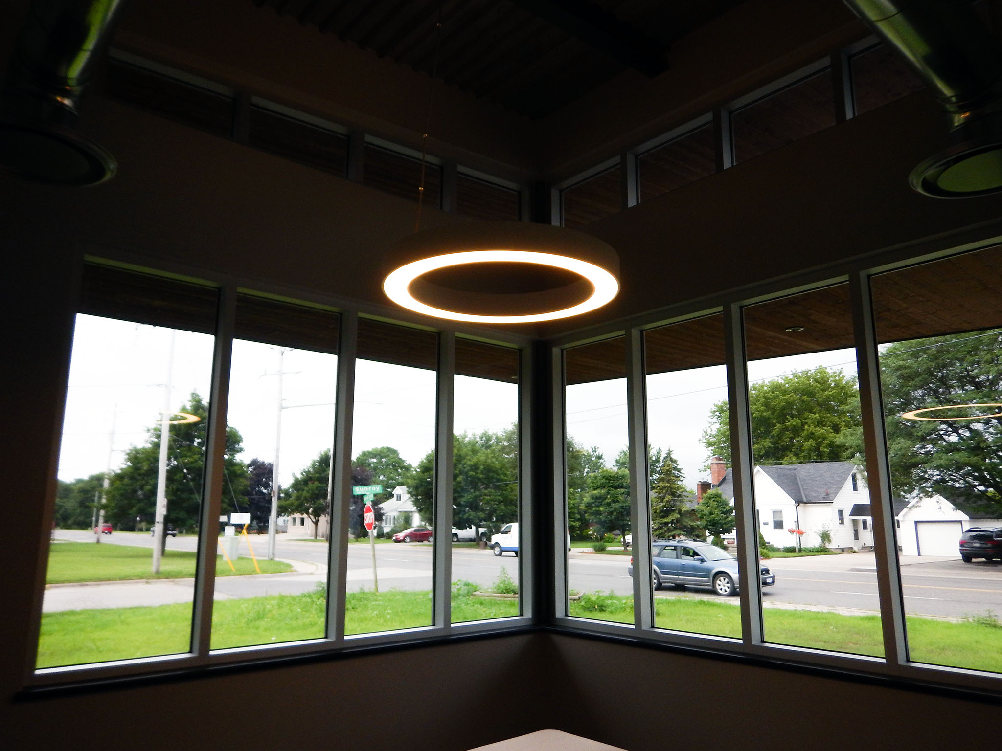 L'Arche 4 Interior view from corner windows of the L’Arche Gathering Facility with circular LED light above and street outside.