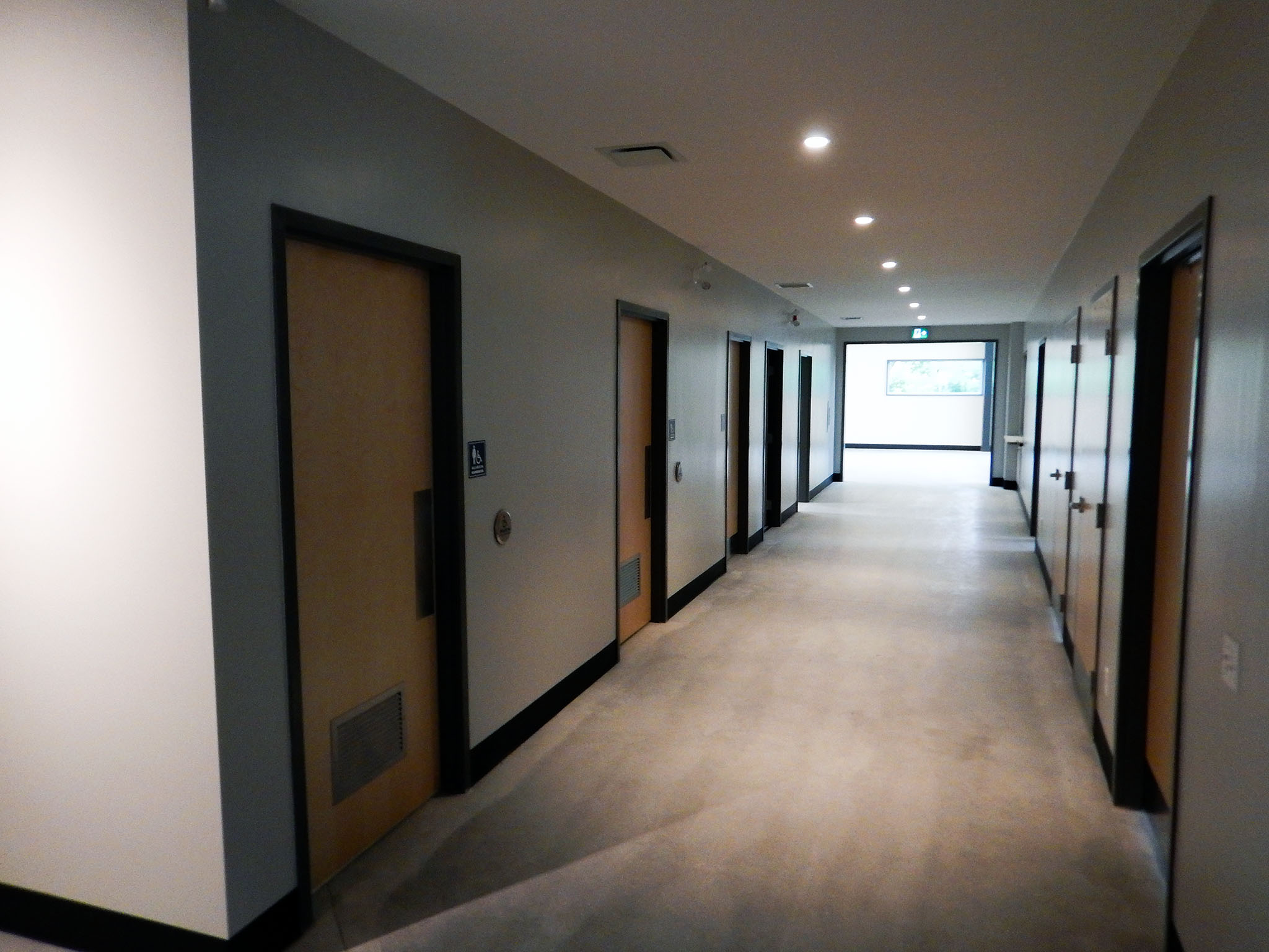 L'Arche 5 Interior hallway at the L’Arche Gathering Facility with multiple wooden doors and overhead recessed lighting.
