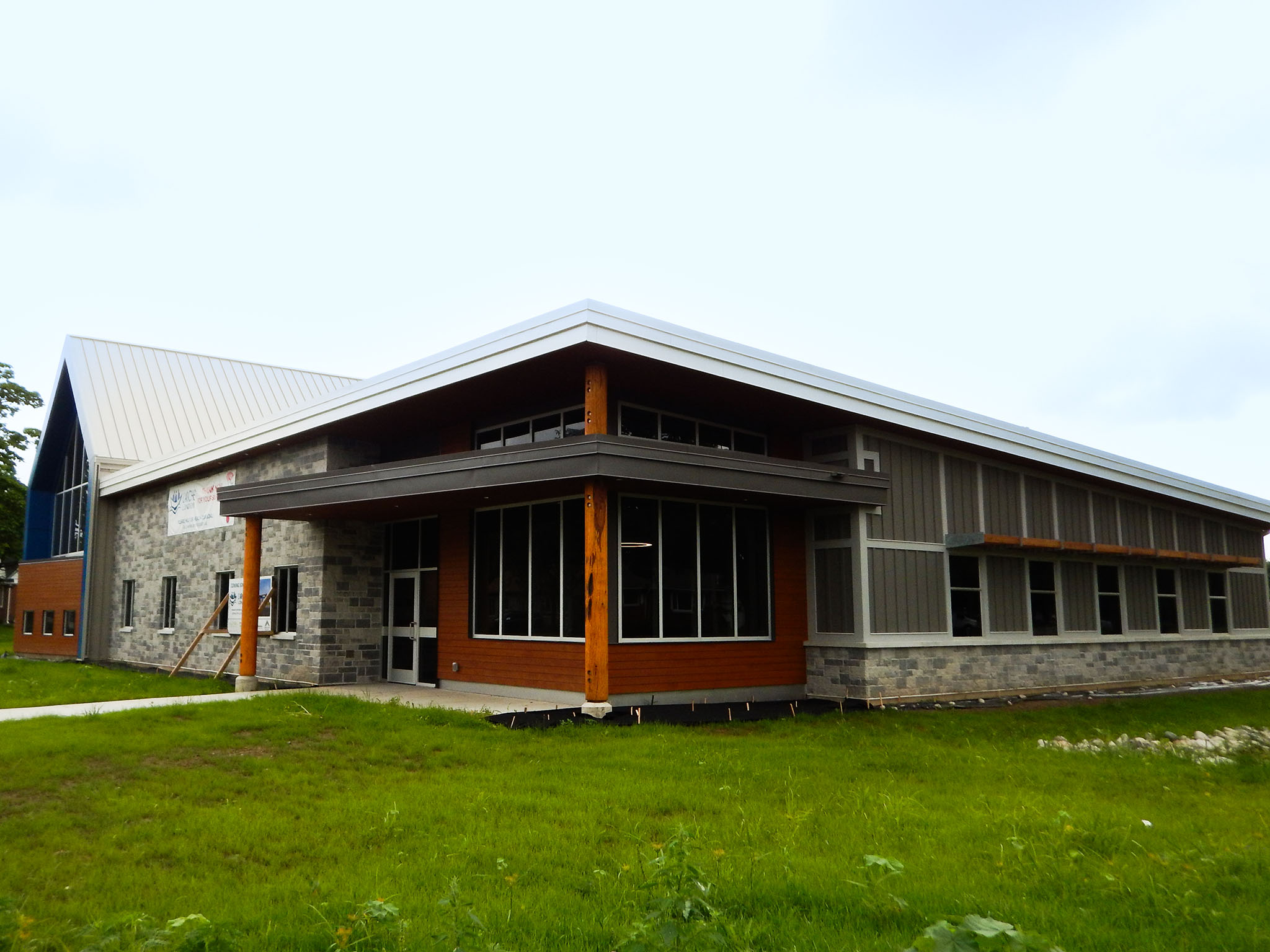L'Arche 9 Exterior view of the L’Arche Community Gathering Facility with stone and wood siding, large windows, and metal roof.