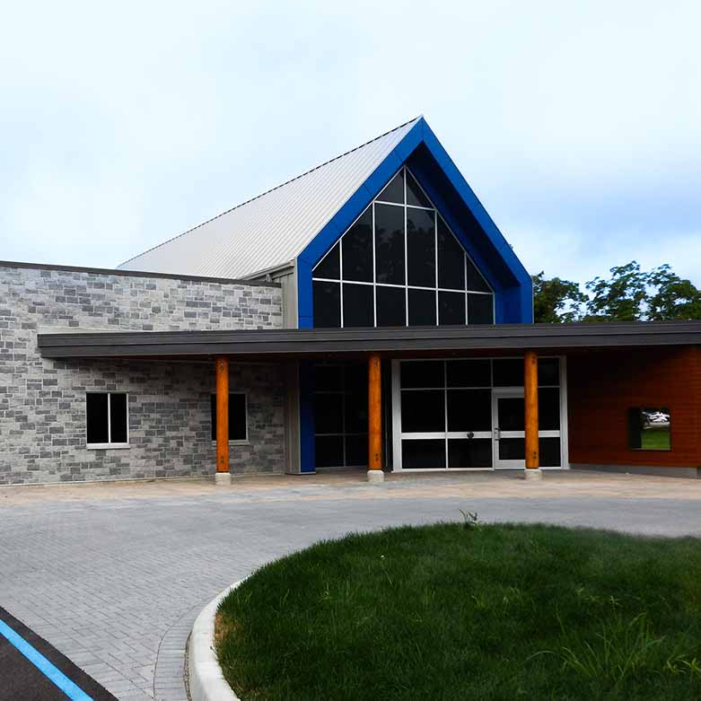 Front view of the L’Arche Community Gathering Facility with stone façade, blue gabled trim, and wood columns at entry.
