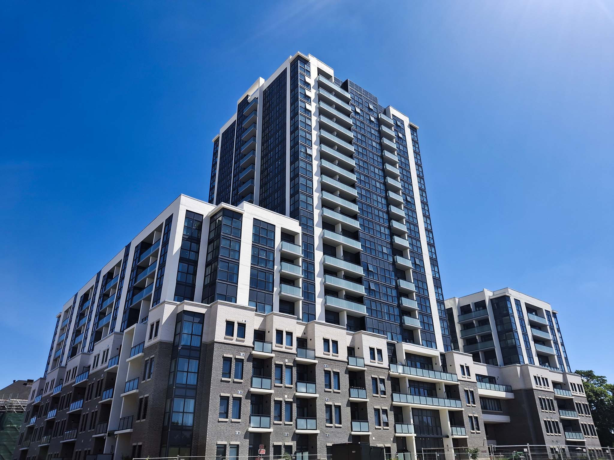 Exterior view of SOHOSQ’s residential tower and podium with glass balconies against a clear blue sky.