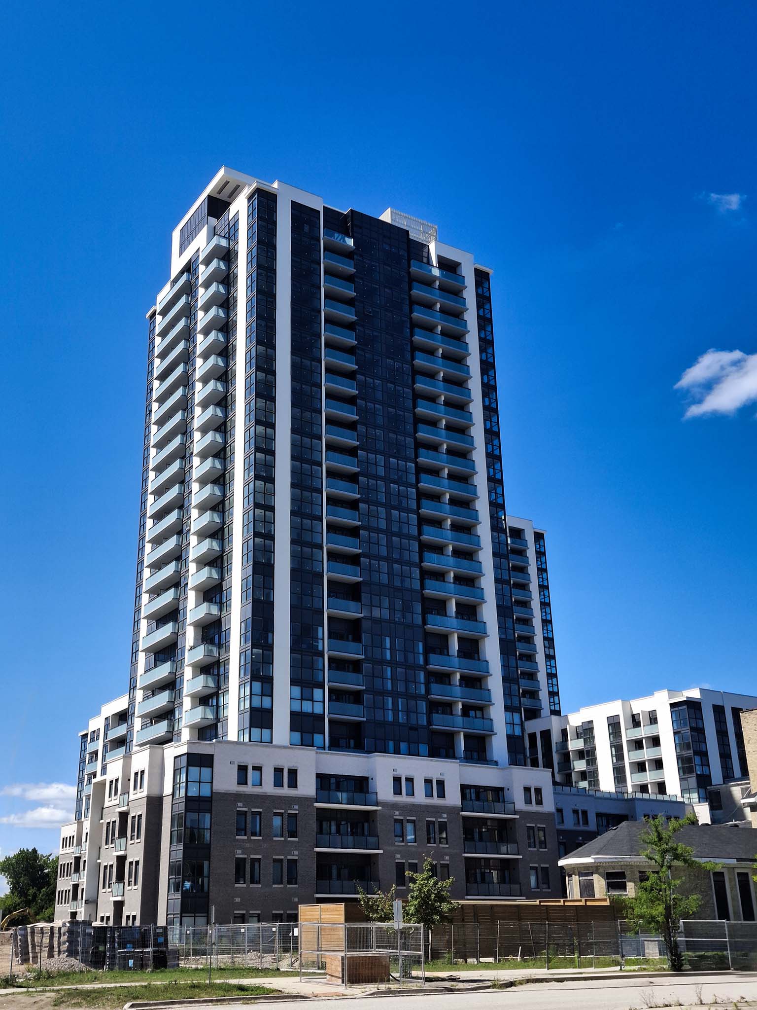 Street-level view of SOHOSQ’s residential tower with glass balconies and podium, set against a clear blue sky.