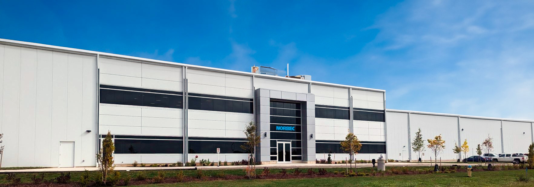 Norbec Industrial 11 Front elevation of Norbec’s Strathroy manufacturing facility with light gray metal panels, black window bands, and landscaped frontage.