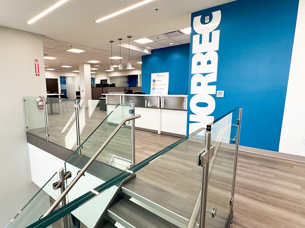 Norbec Industrial 9 Interior of Norbec’s Strathroy office with glass stair railing, blue feature wall with Norbec logo, and open workstations.
