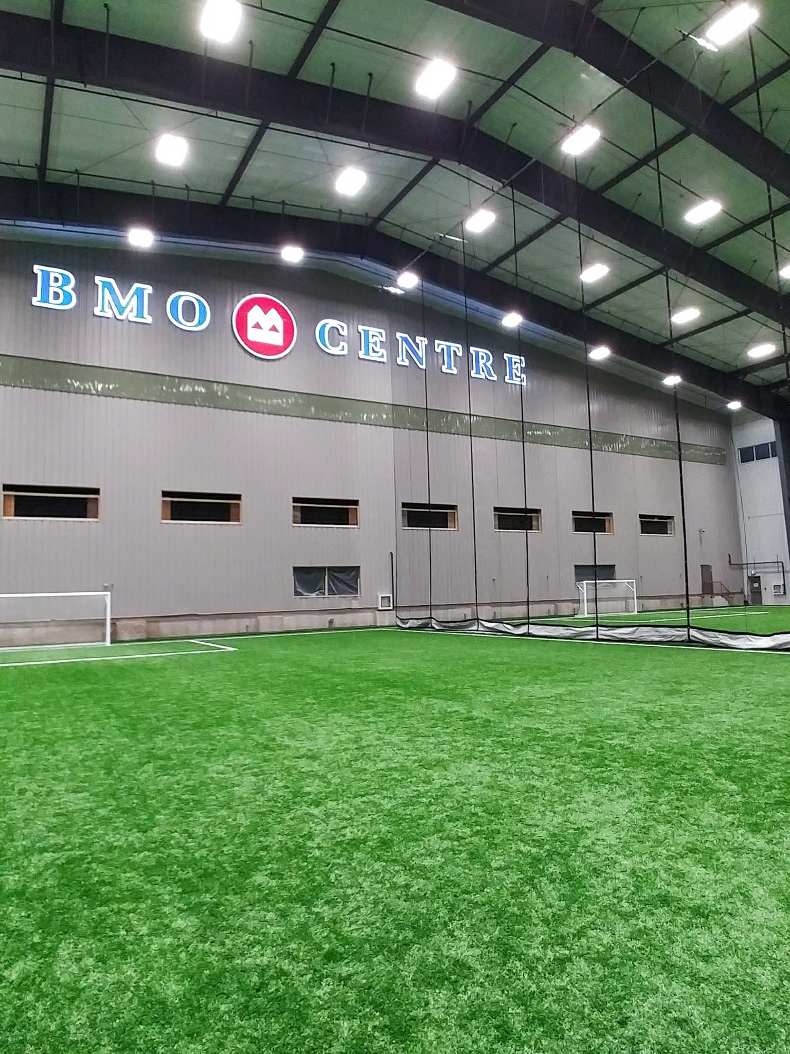 BMO Centre 13 Indoor turf field with bright overhead lighting and the BMO Centre wall signage visible above the playing area.