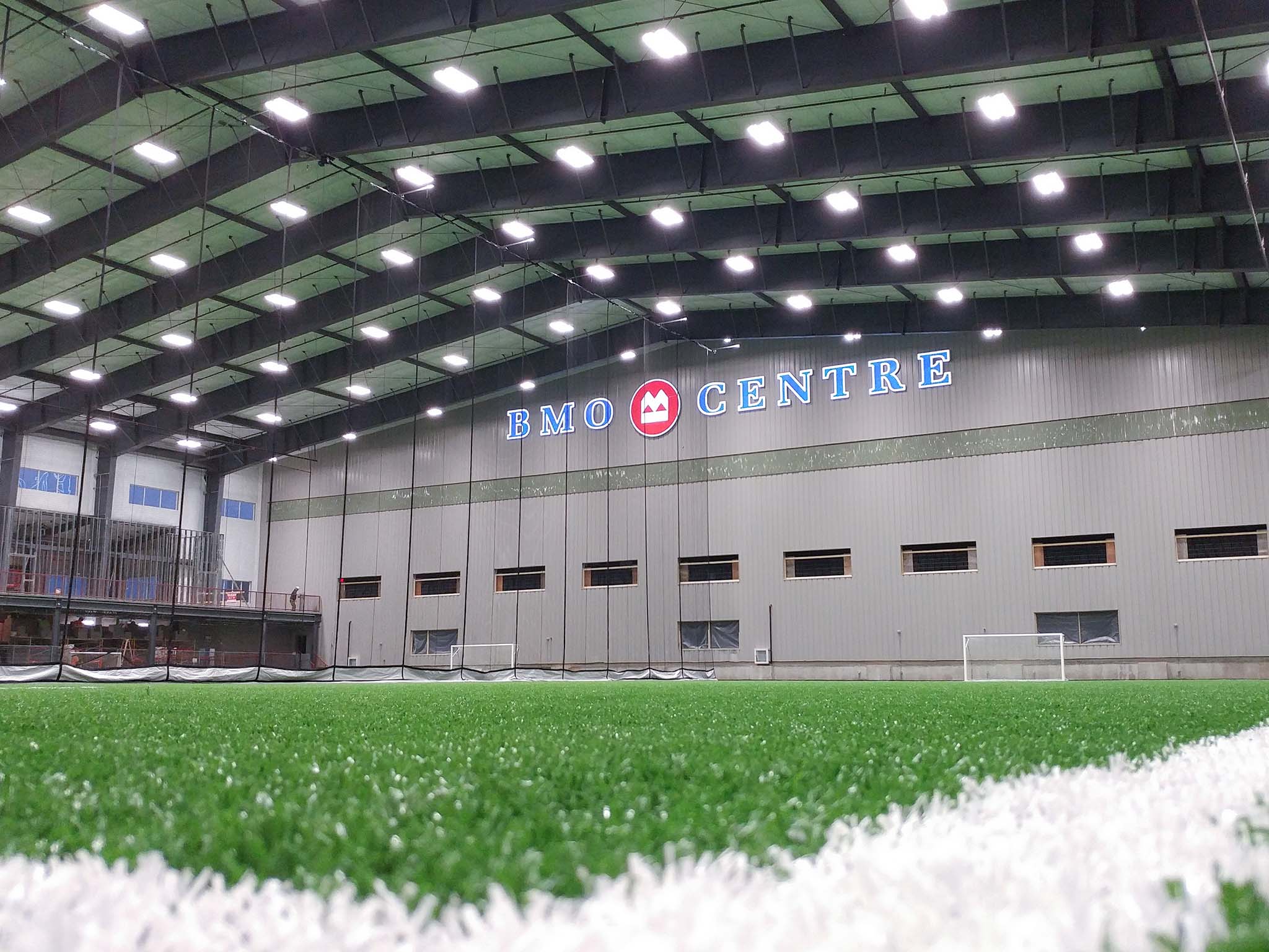 BMO Centre (6) Interior of the BMO Centre showing the indoor turf field, high roof structure, bright lighting, and wall signage.