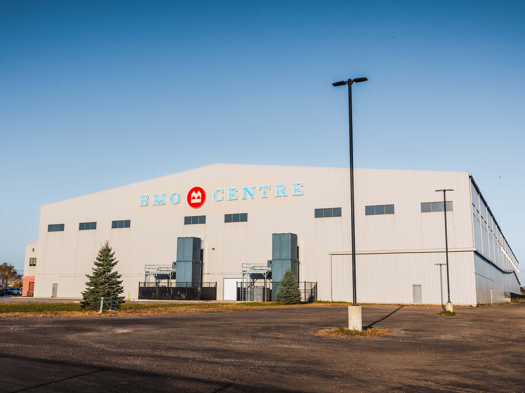 b Exterior of the BMO Centre building on a clear day, showing the large metal facade, signage, and empty parking area.