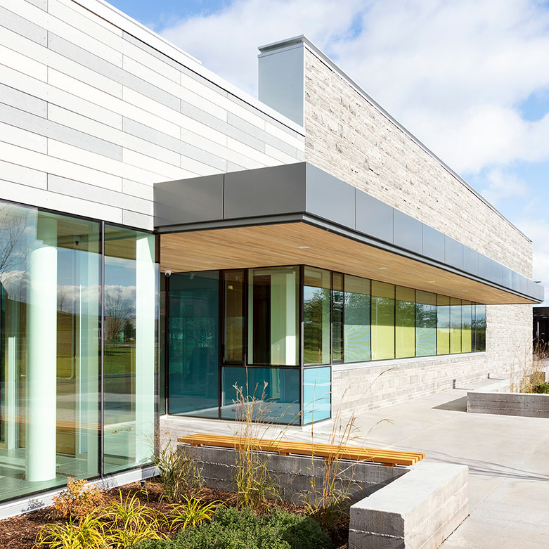 Carpenter's Union Local 249 Exterior of a modern single-storey building with glass walls, light stone cladding, landscaped plantings, and a concrete walkway under a blue sky.