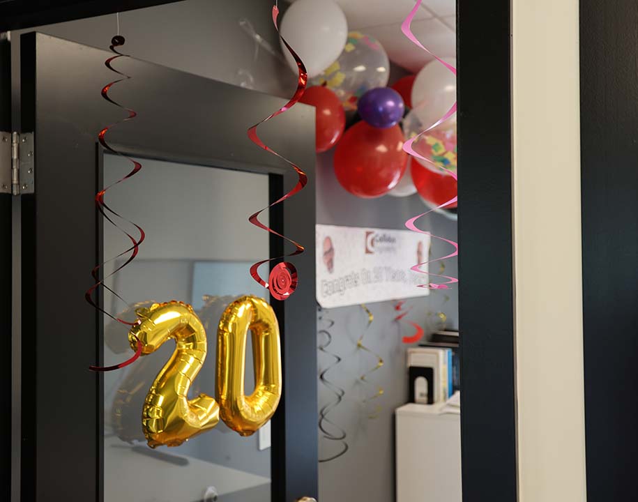 Gold 20 balloons hang from a decorated office doorway for a Callidus anniversary celebration.