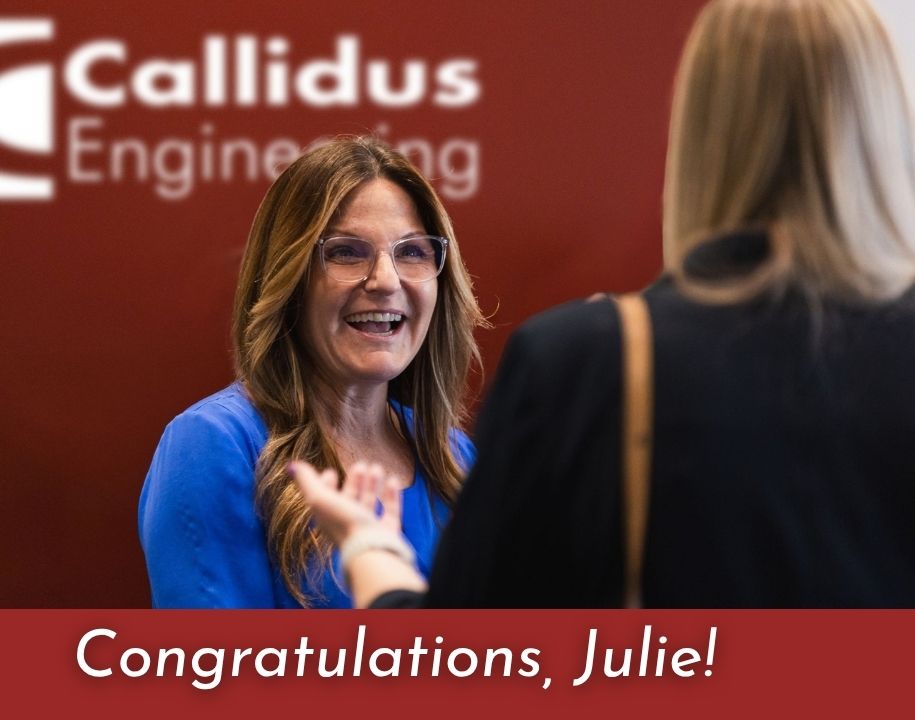 Julie Pepper smiles while speaking with a colleague in front of a Callidus Engineering wall.