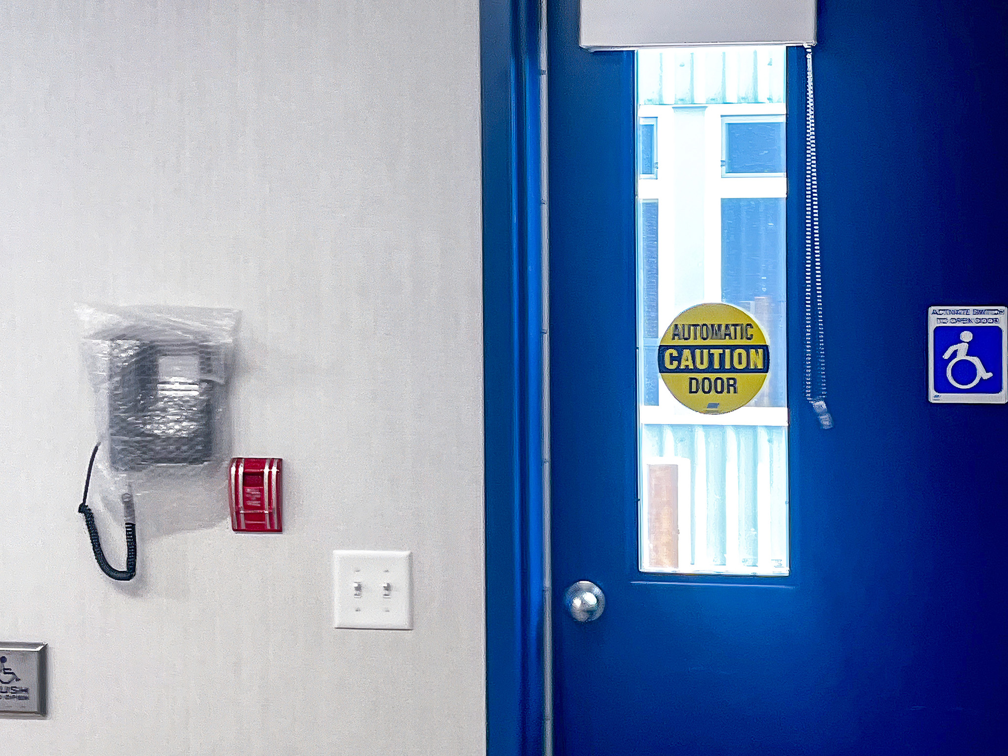 Beckwith Public School (3) Blue portable classroom door with an automatic door warning, accessibility sign, wall-mounted handset, and fire alarm pull station.