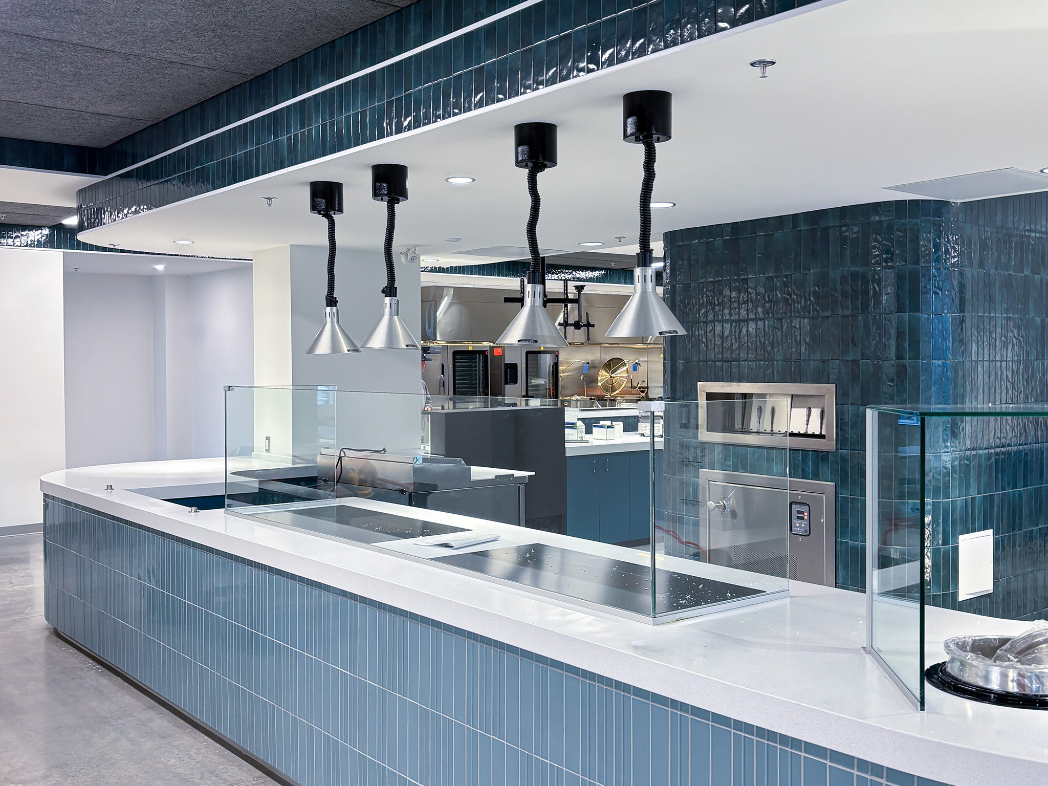 Rodzik Hall (2) Food service counter with blue tile, glass partitions, hanging heat lamps, and commercial kitchen equipment.