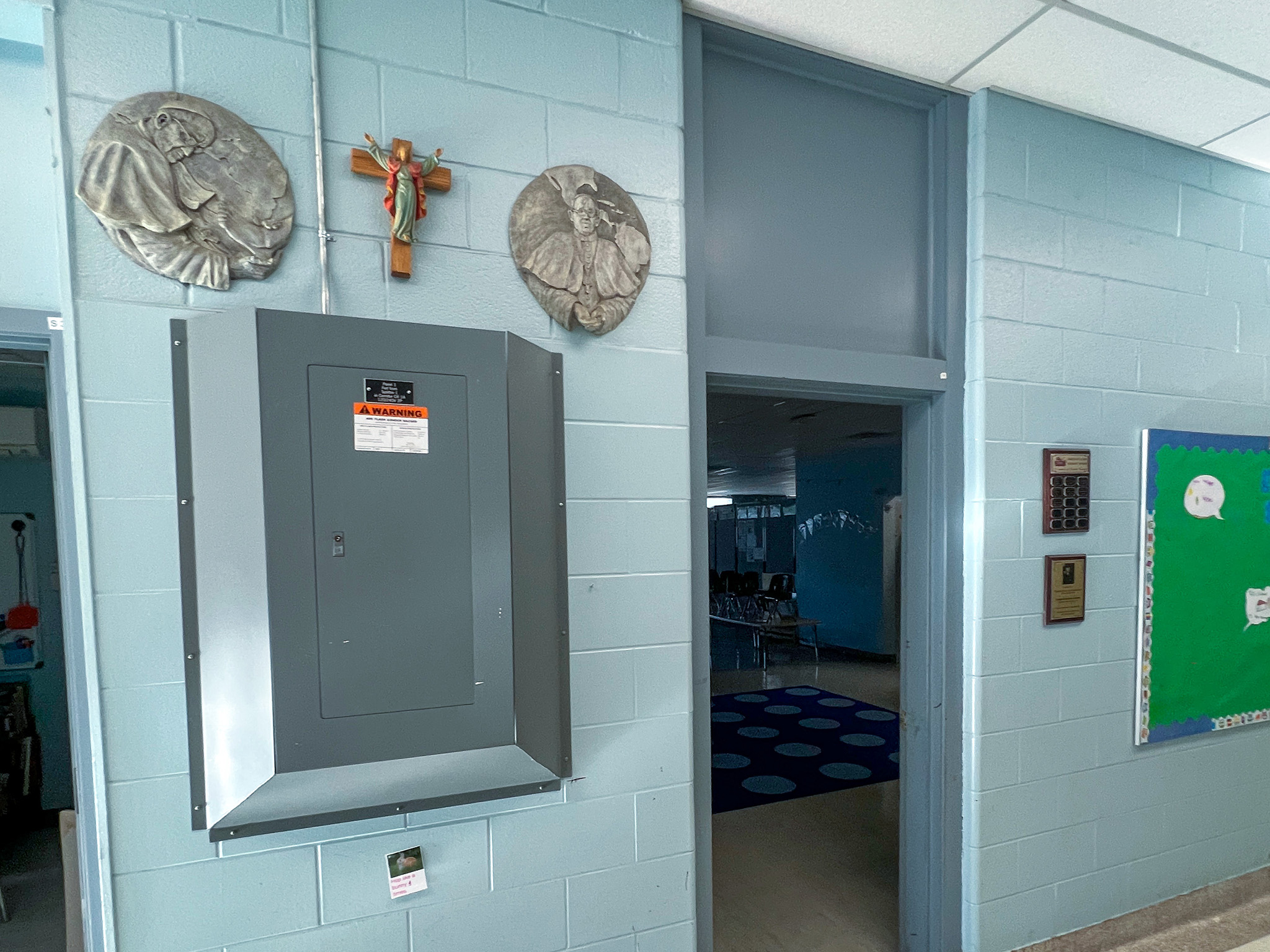 St. Anne French Immmersion Catholic Elementary School (1) School hallway with an electrical panel, religious plaques, a crucifix, and an open classroom doorway.