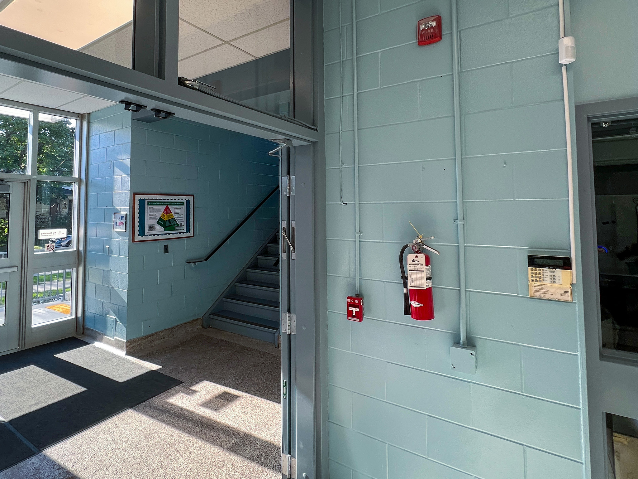 St. Anne French Immmersion Catholic Elementary School (3) School vestibule doorway with an overhead door closer, fire alarm devices, security keypad, and fire extinguisher.