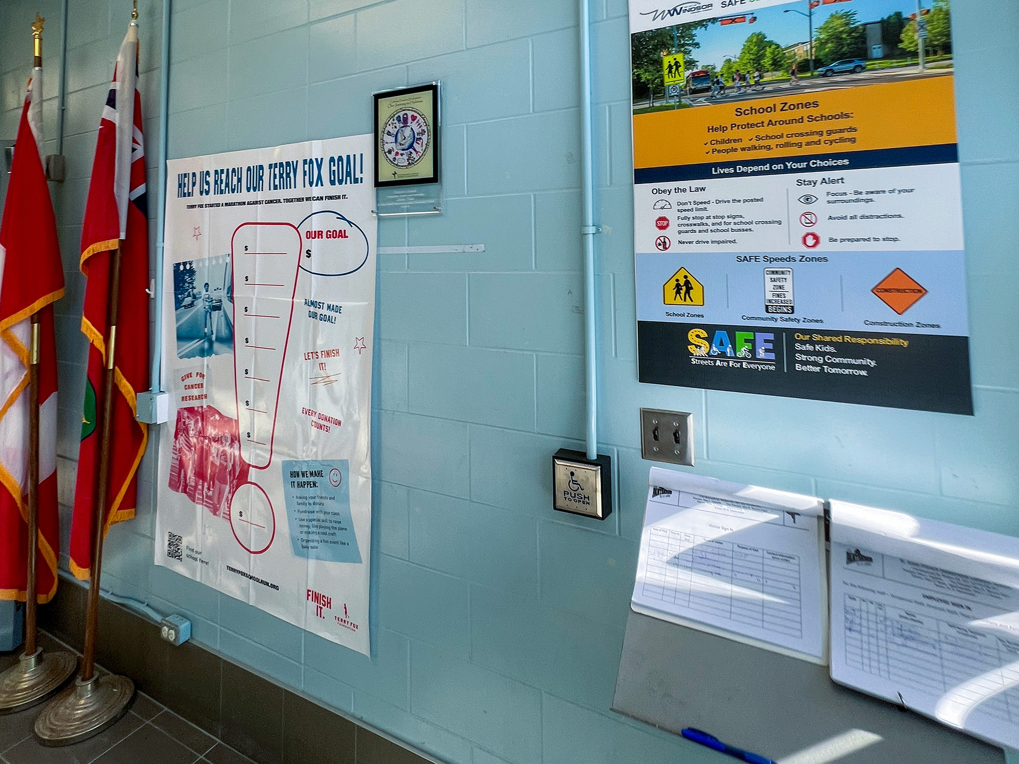 St. Anne French Immmersion Catholic Elementary School (4) School entrance wall with flags, safety posters, an automatic door push button, and visitor sign-in sheets.