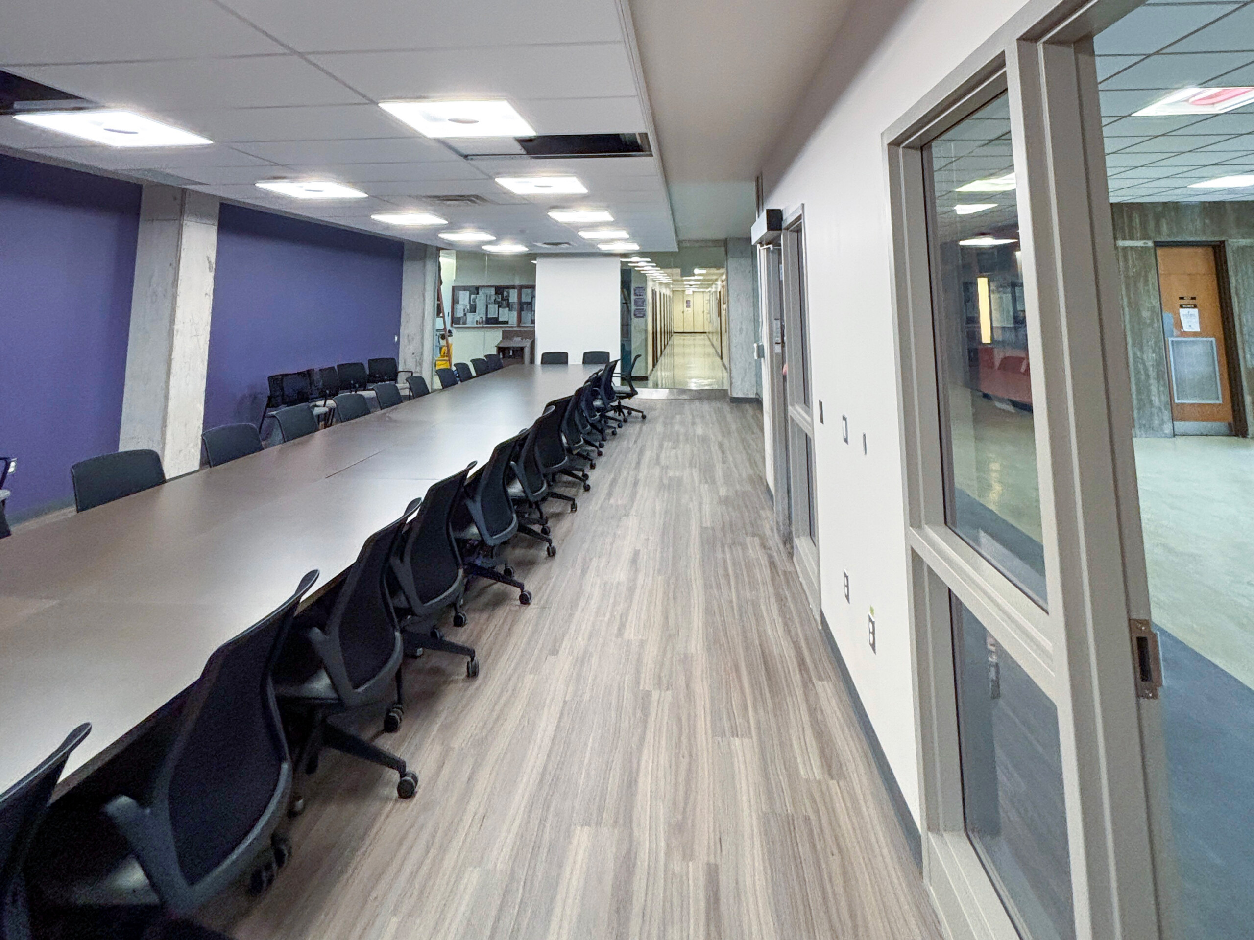 Western University SSC (2) Long conference table with rolling chairs beside a purple wall, with glass partitions and a corridor beyond.