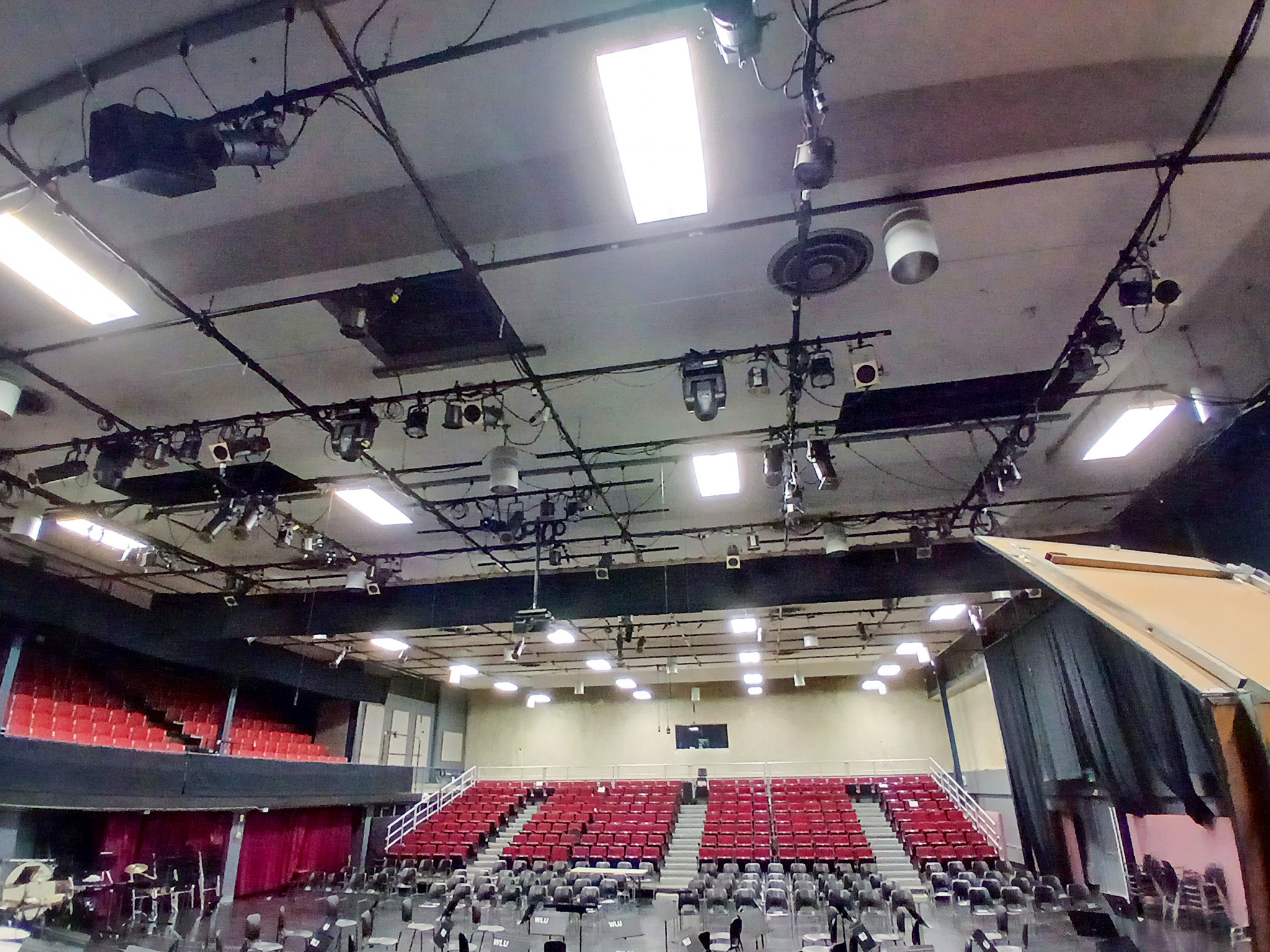 Wilfrid Laurier University Theatre Auditorium (1) View from the stage showing red auditorium seating, overhead theatrical lighting, suspended equipment, and ceiling rigging.