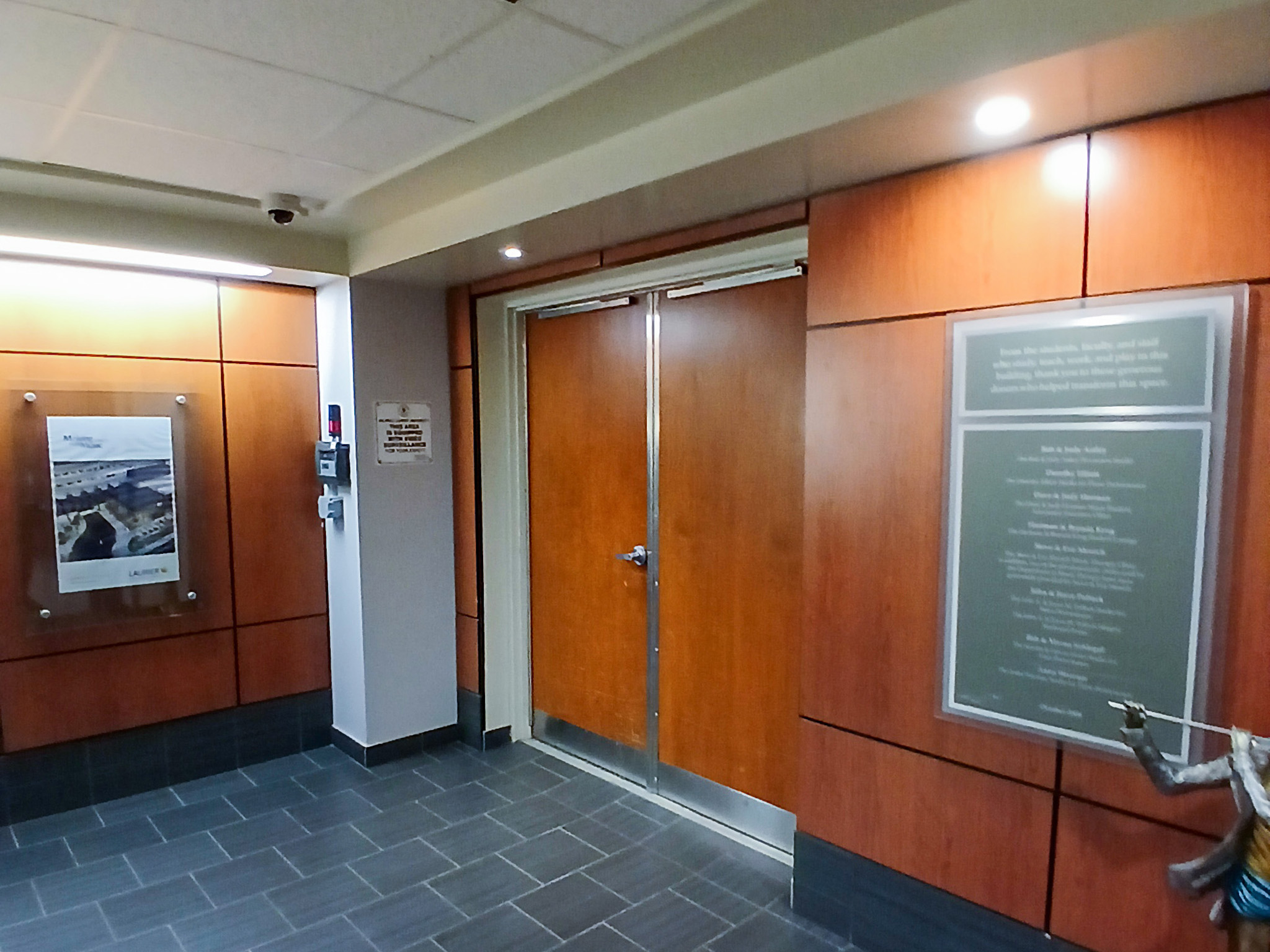Wilfrid Laurier University Theatre Auditorium (2) Wood-panelled theatre entrance with double doors, tiled flooring, overhead lighting, and wall-mounted plaques.